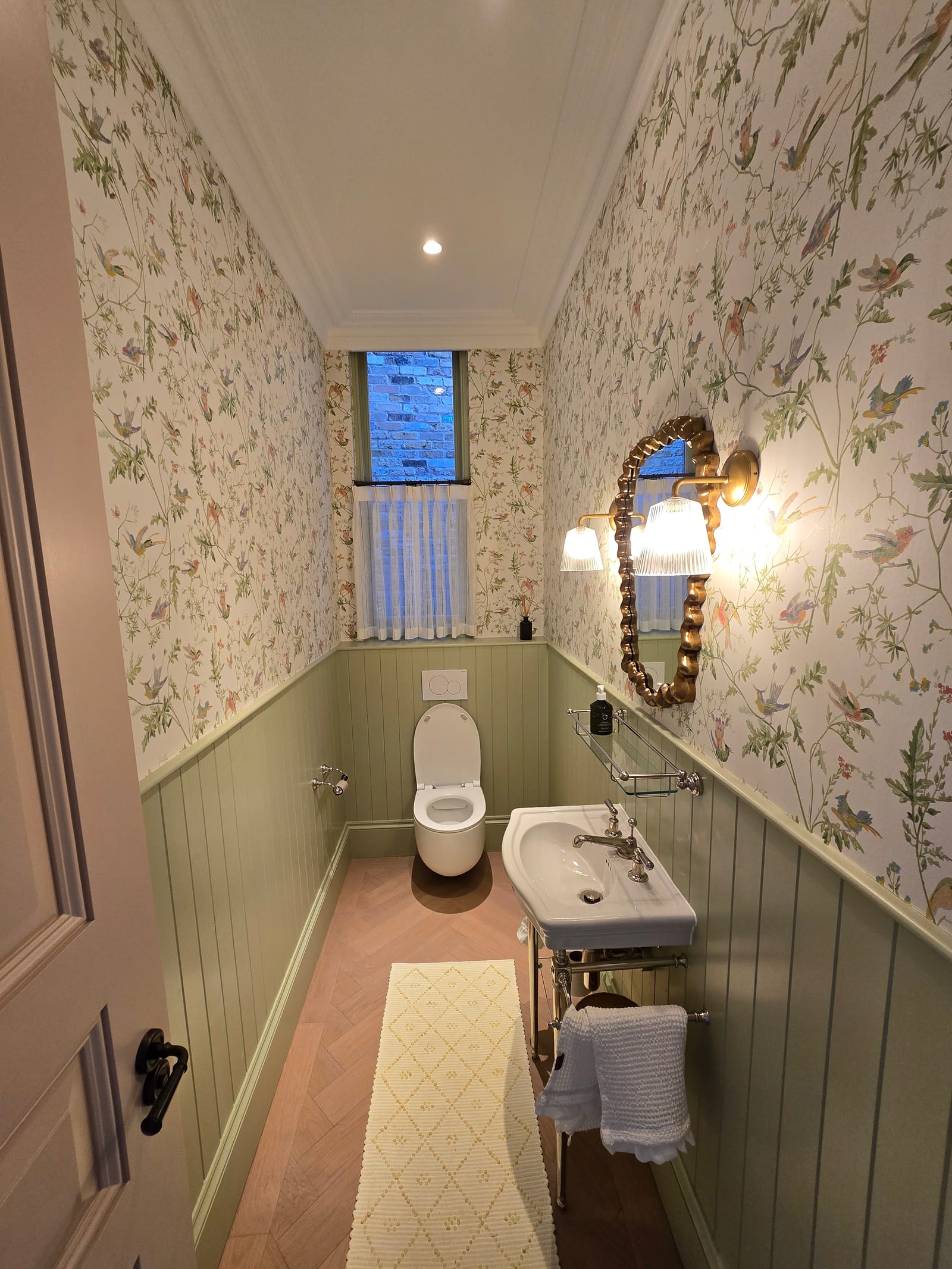 Cloakroom with bird-and-botanical wallpaper on walls and ceiling and sage painted panelling.