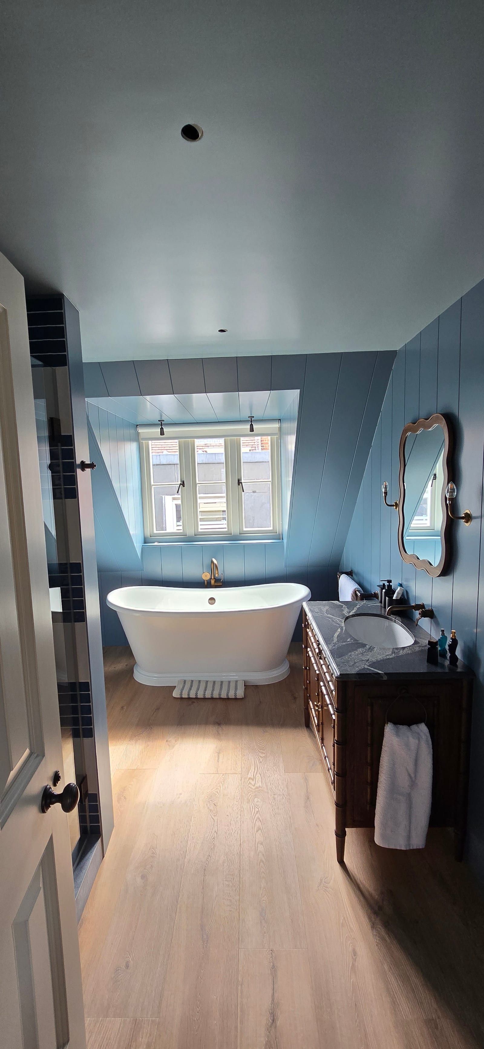Ensuite bathroom with blue painted panelling, freestanding bath, brass fittings, and oak floor.