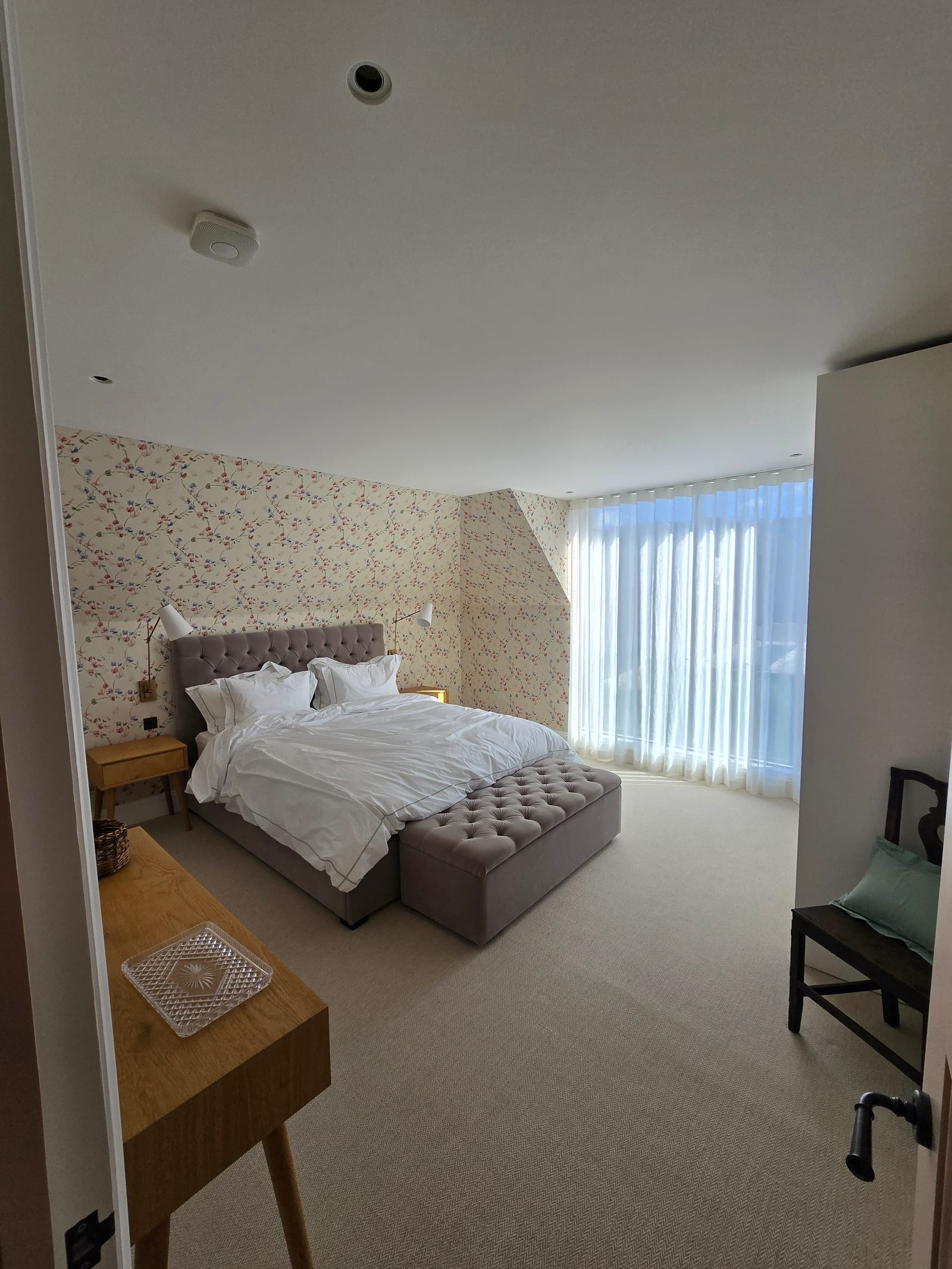 Bedroom finished with climbing floral wallpaper, tufted headboard, and soft neutral bedding.