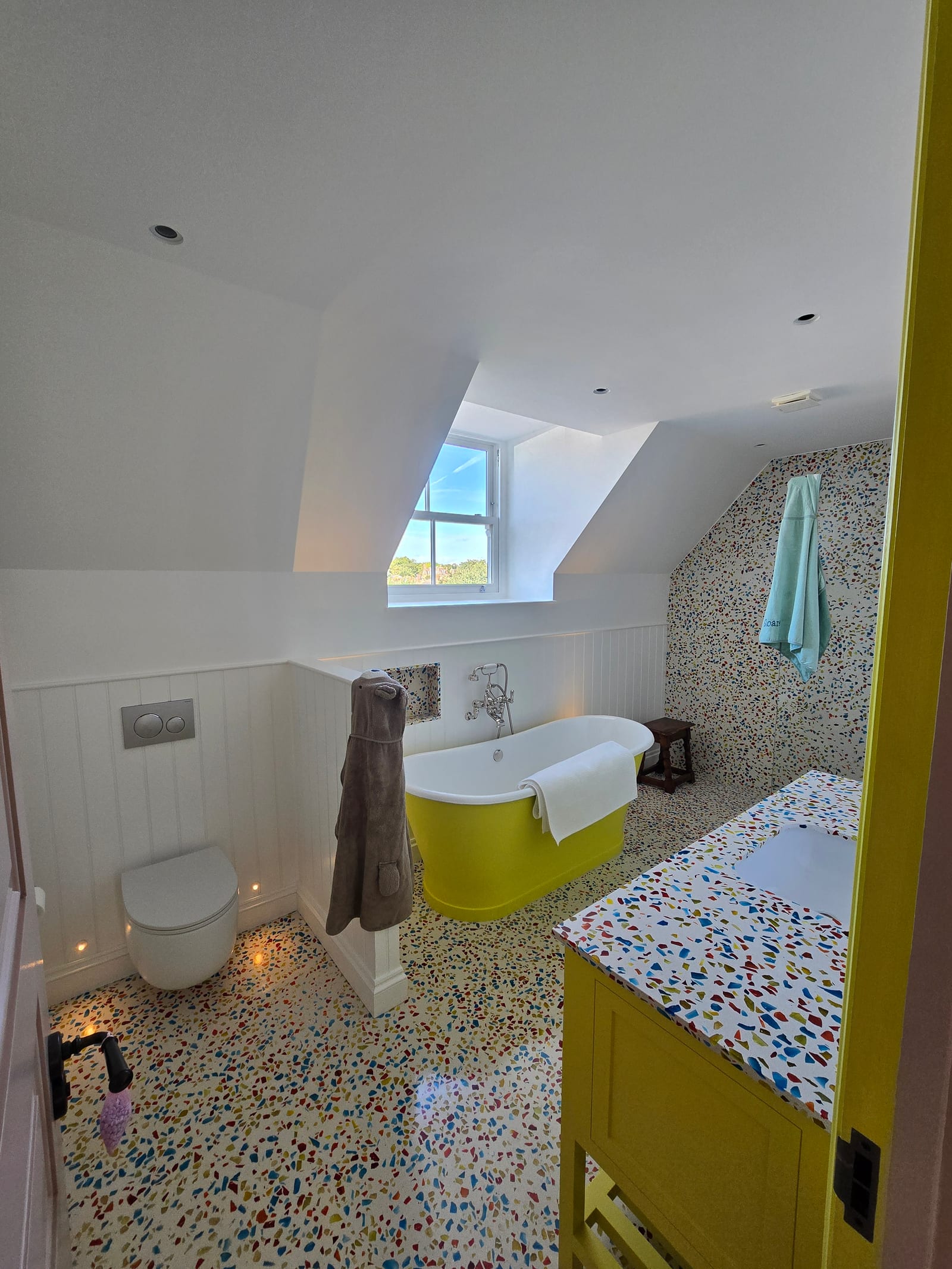 Bathroom with freestanding chartreuse bath, confetti terrazzo surfaces, and painted panelling.