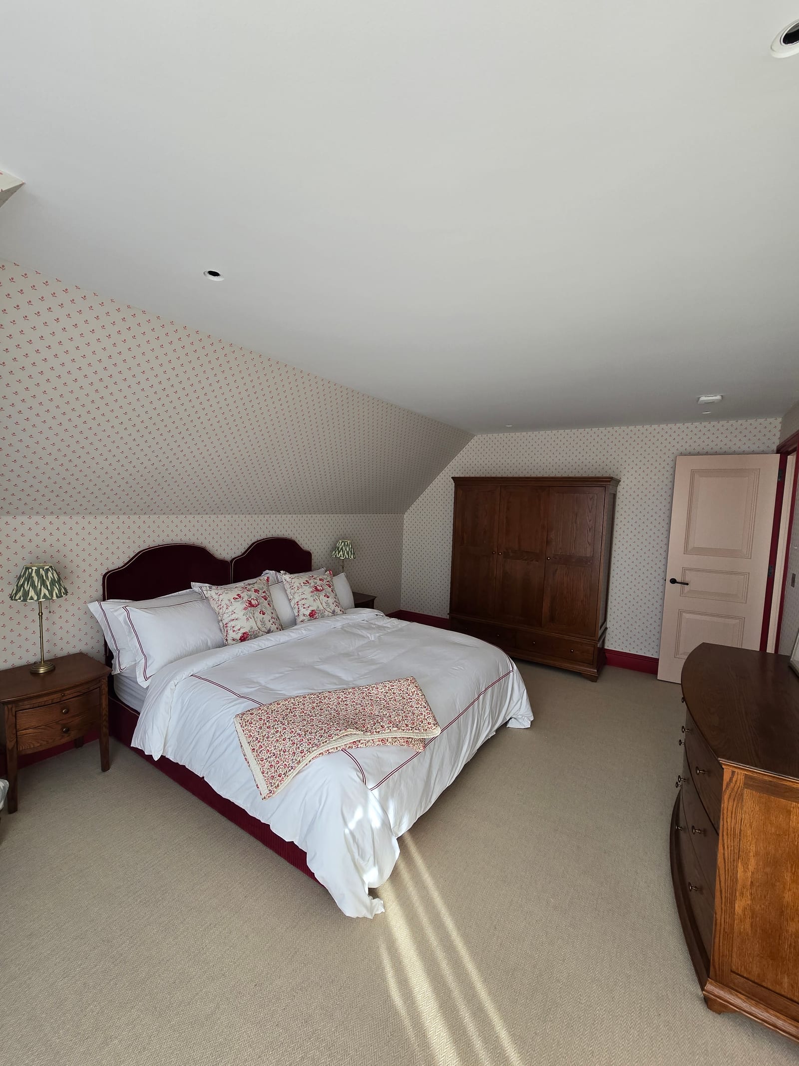 Bedroom with small-scale cottage-print wallpaper, burgundy headboard, and painted woodwork.