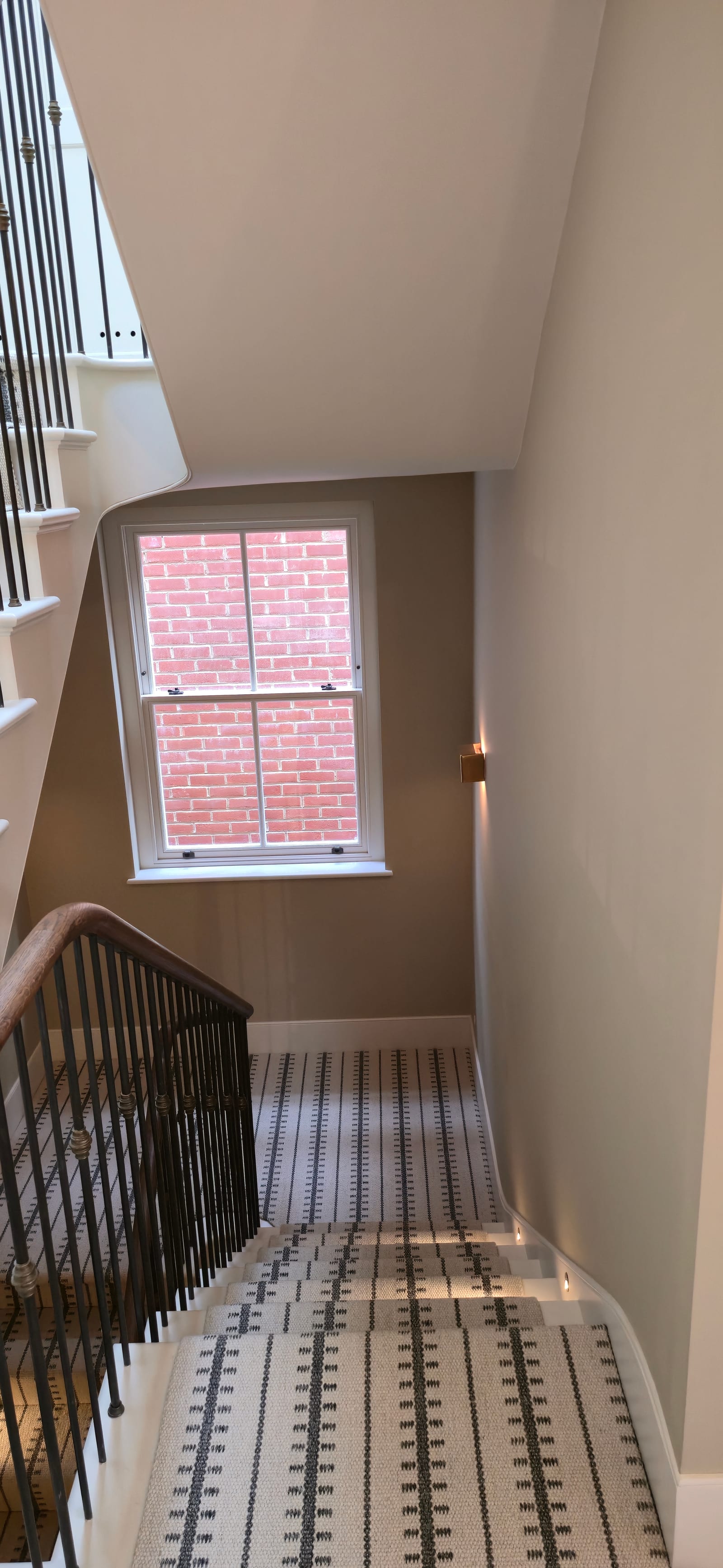 Curved staircase with patterned runner, black spindles, oak handrail, and painted walls.