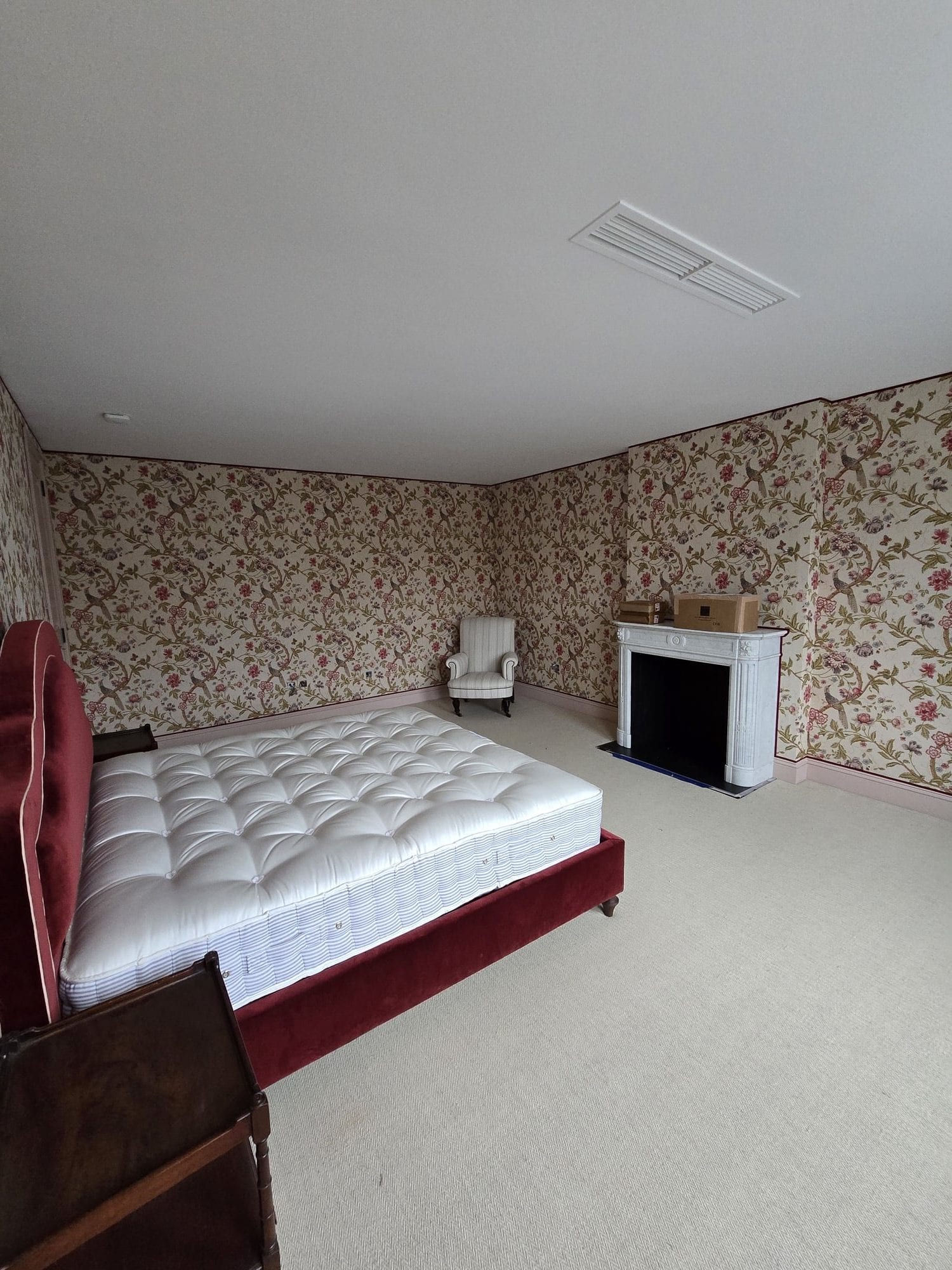 Bedroom with patterned wallpaper, fireplace, and light carpet.