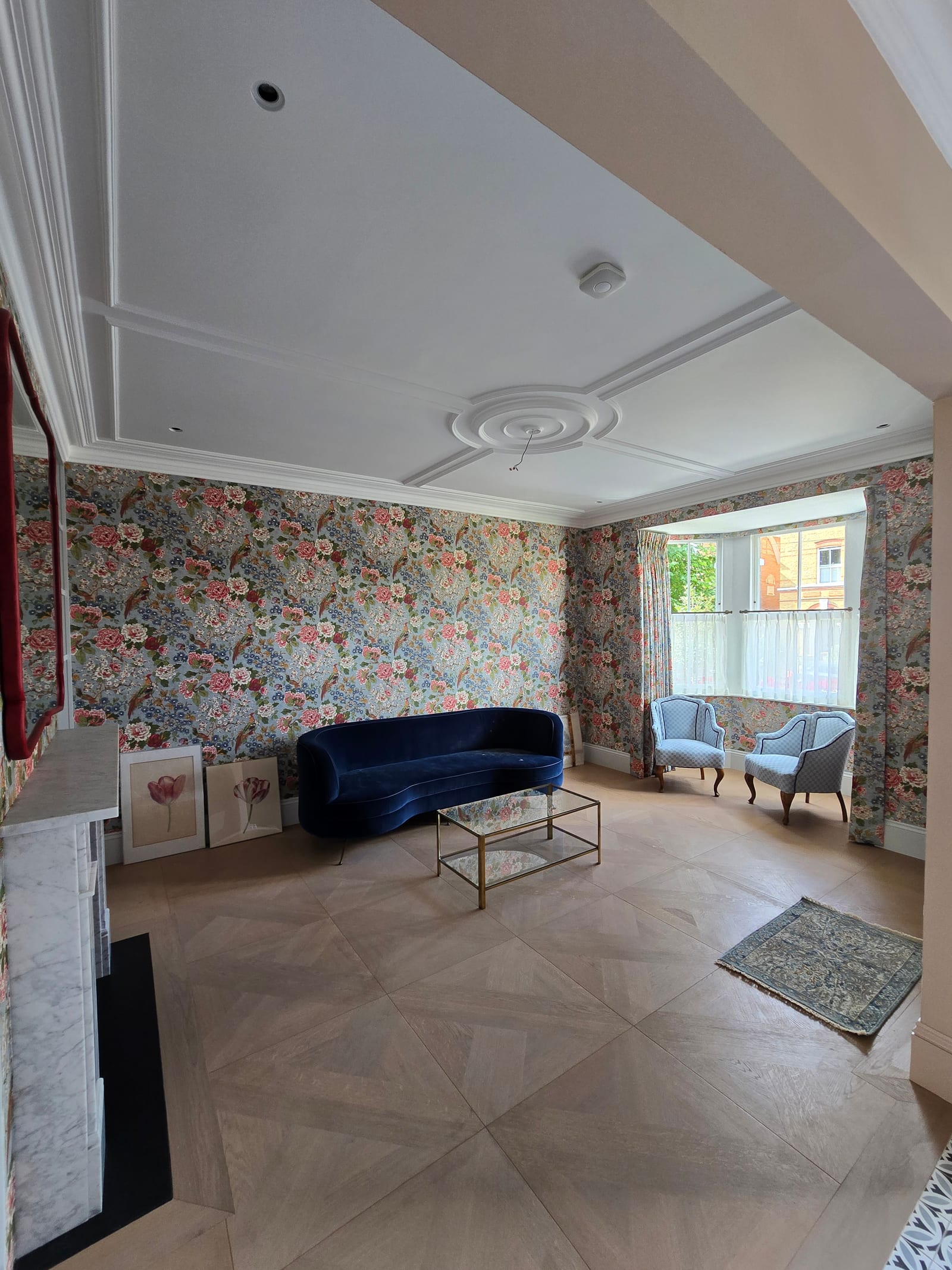 Reception room with large-scale floral wallpaper, white painted panelling, and decorative mouldings.
