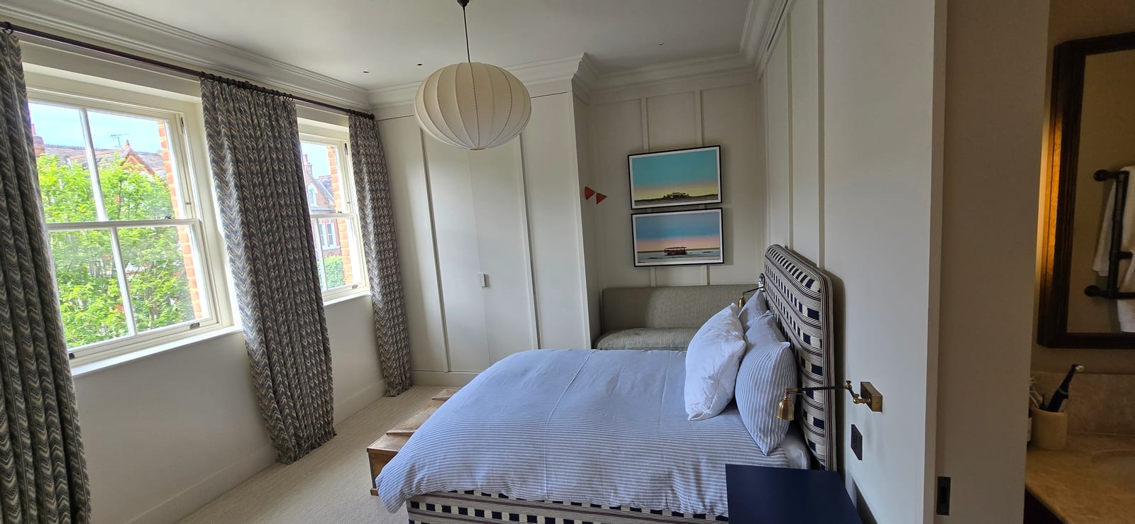 Bedroom with white wall panelling, built-in wardrobes, bay windows, and calm neutral finish.