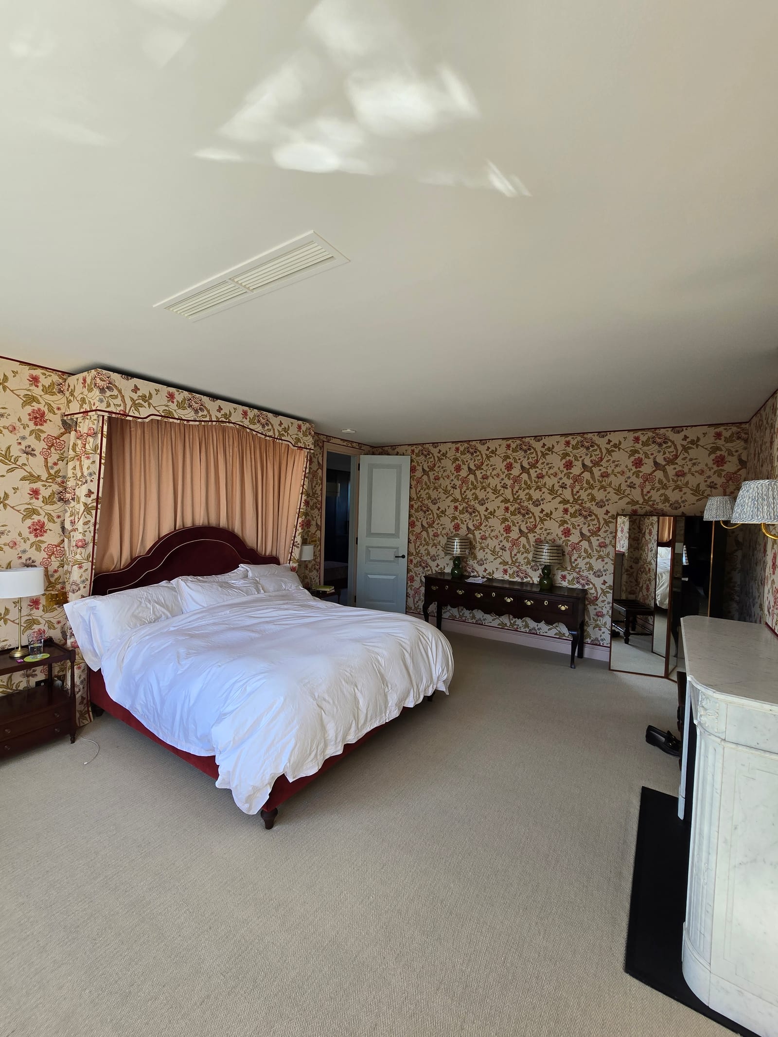 Principal bedroom wrapped in dense rose wallpaper with marble fireplace and painted woodwork.