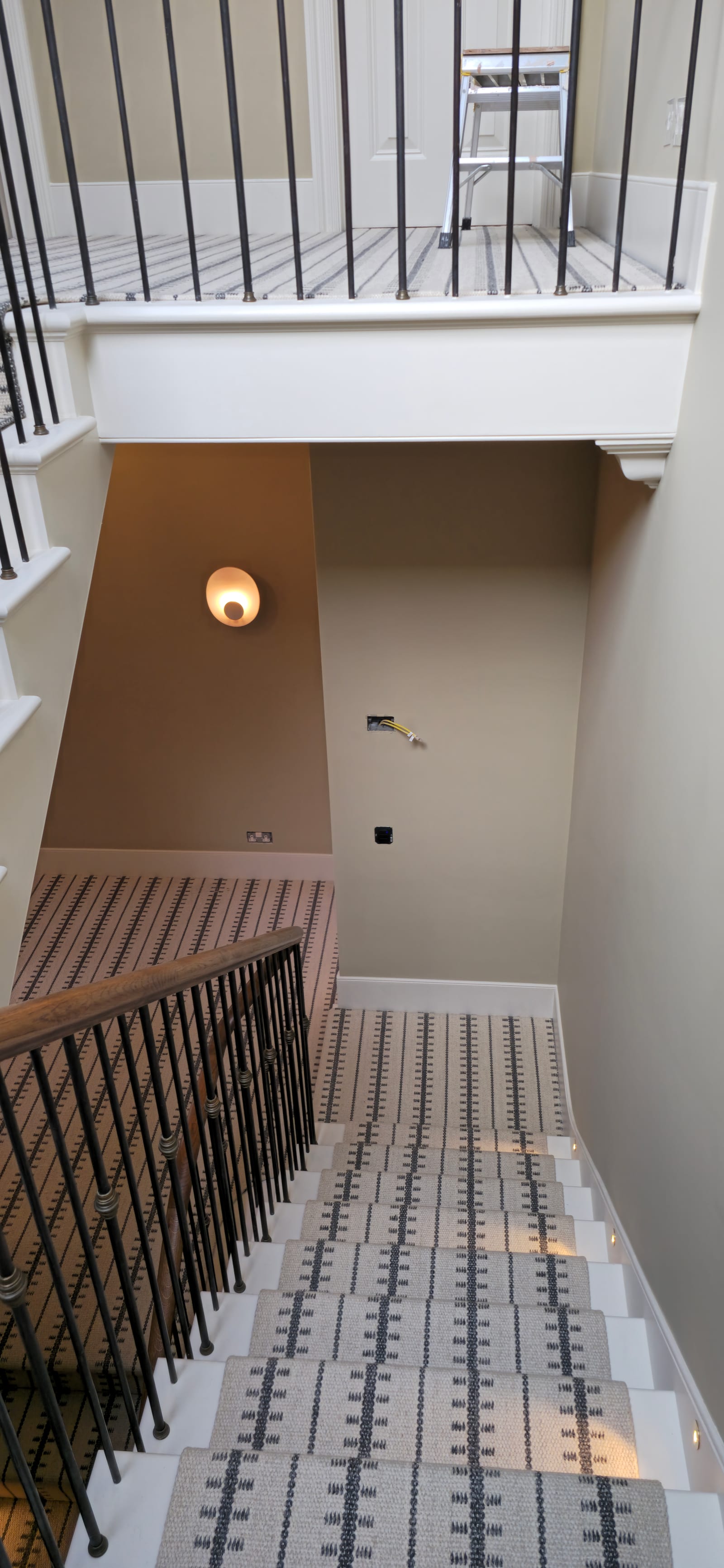 Top-floor staircase with black metal balustrade, geometric runner, and painted walls.