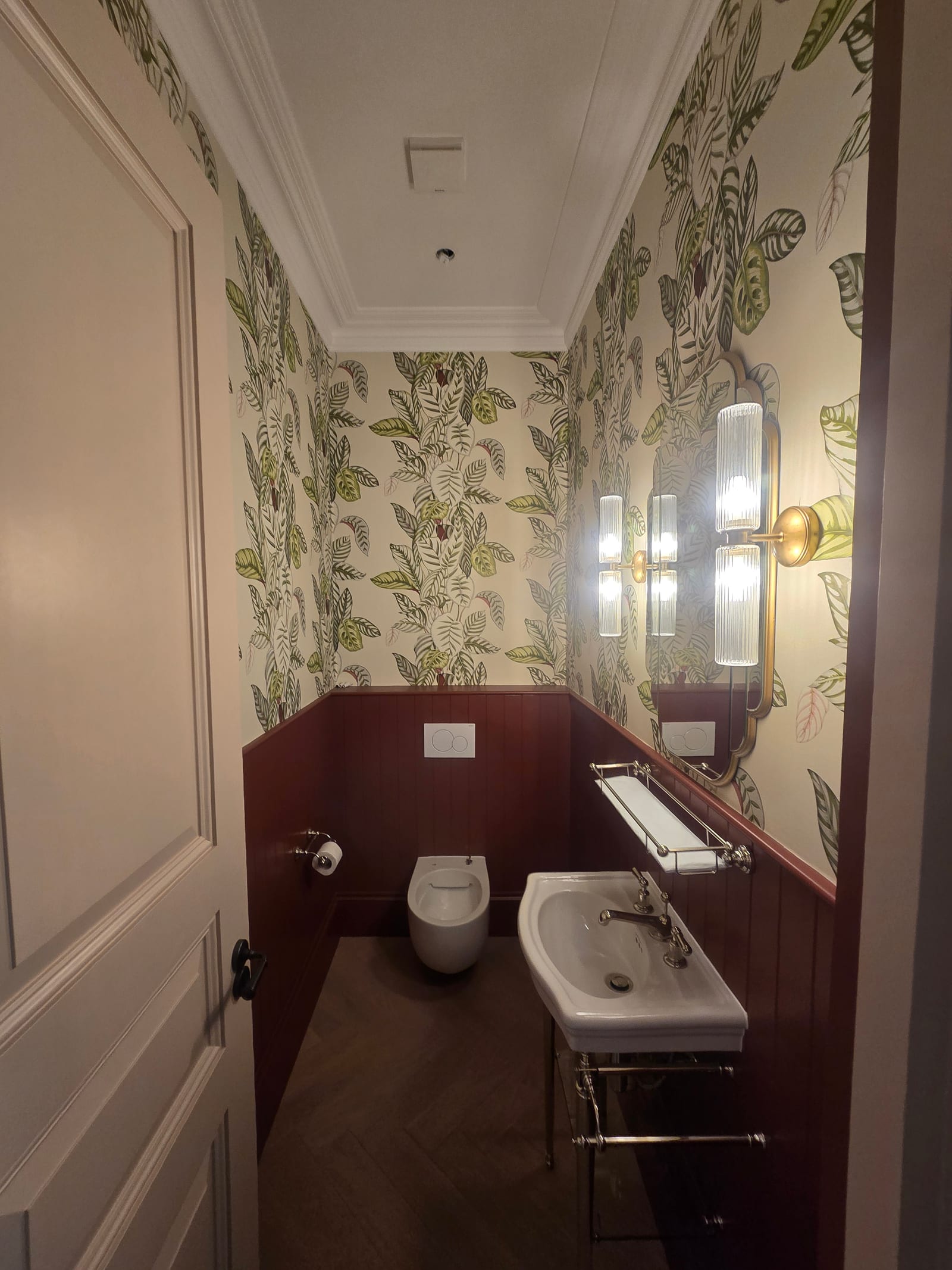 Cloakroom with tropical leaf wallpaper and deep burgundy painted tongue-and-groove panelling.