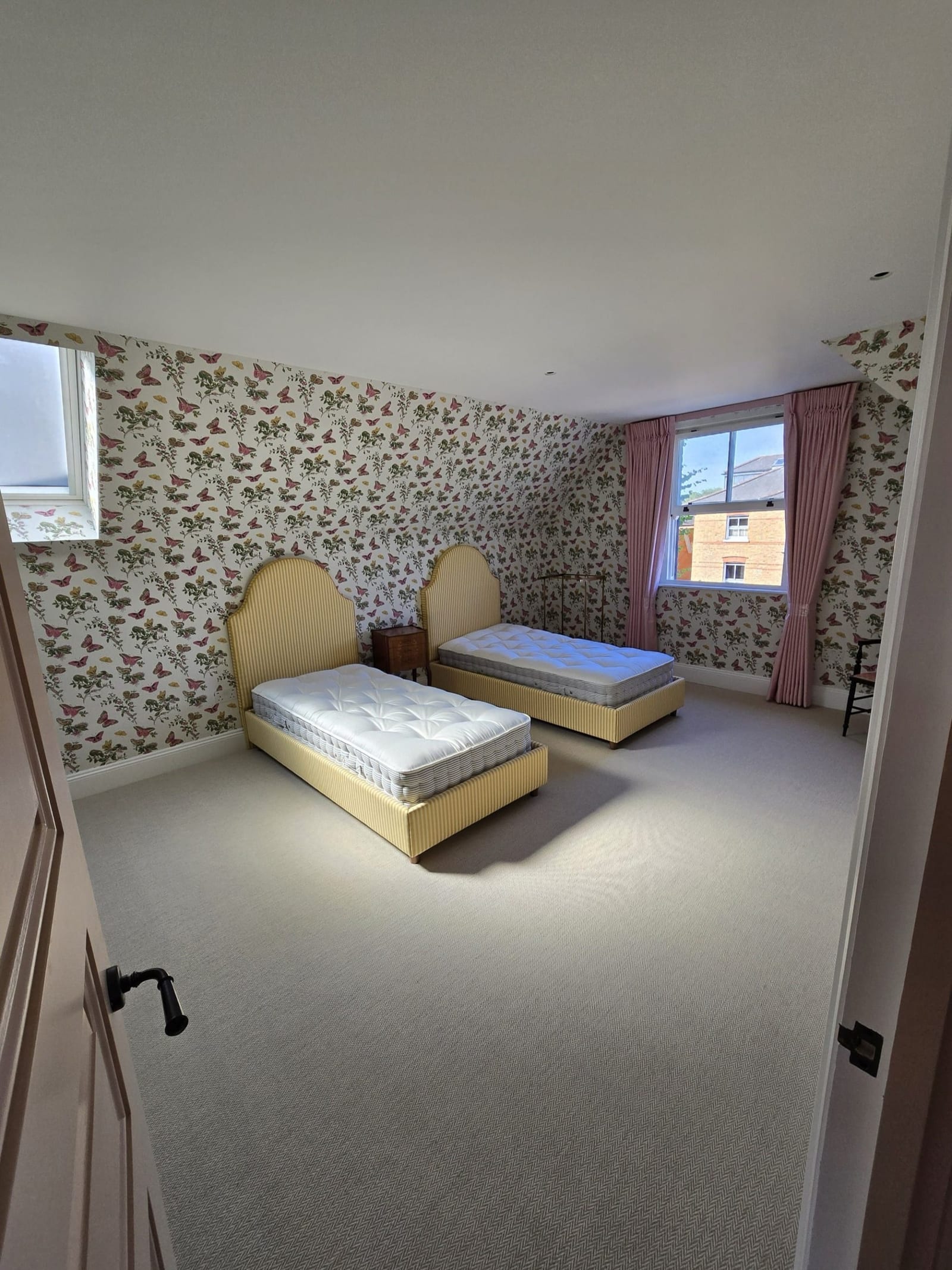Guest bedroom with wallpapered walls, twin beds, and pink curtains.