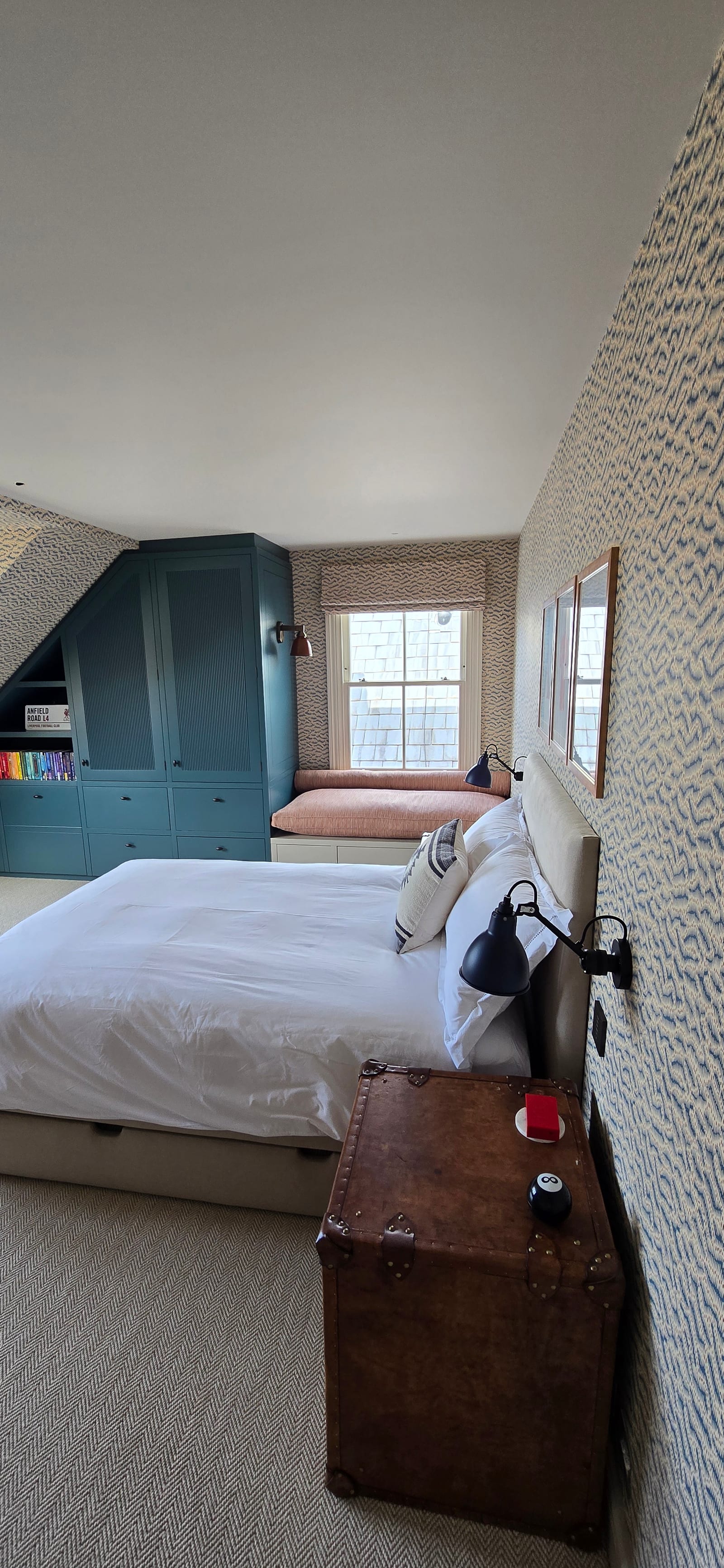 Attic bedroom with blue wave wallpaper on walls and ceiling and teal built-in joinery under the eaves.